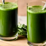 Two glasses of green juice with straws on a wooden tray