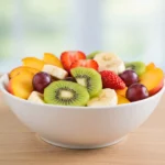 A colorful bowl of easy fruit salad with fresh slices of kiwi, strawberries, banana, and grapes.