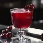 Close-up of cherry juice in a vintage glass with cherries on a metallic surface