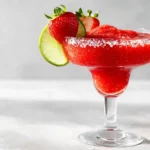 Frozen strawberry margarita in a coupe glass with lime and strawberry garnish